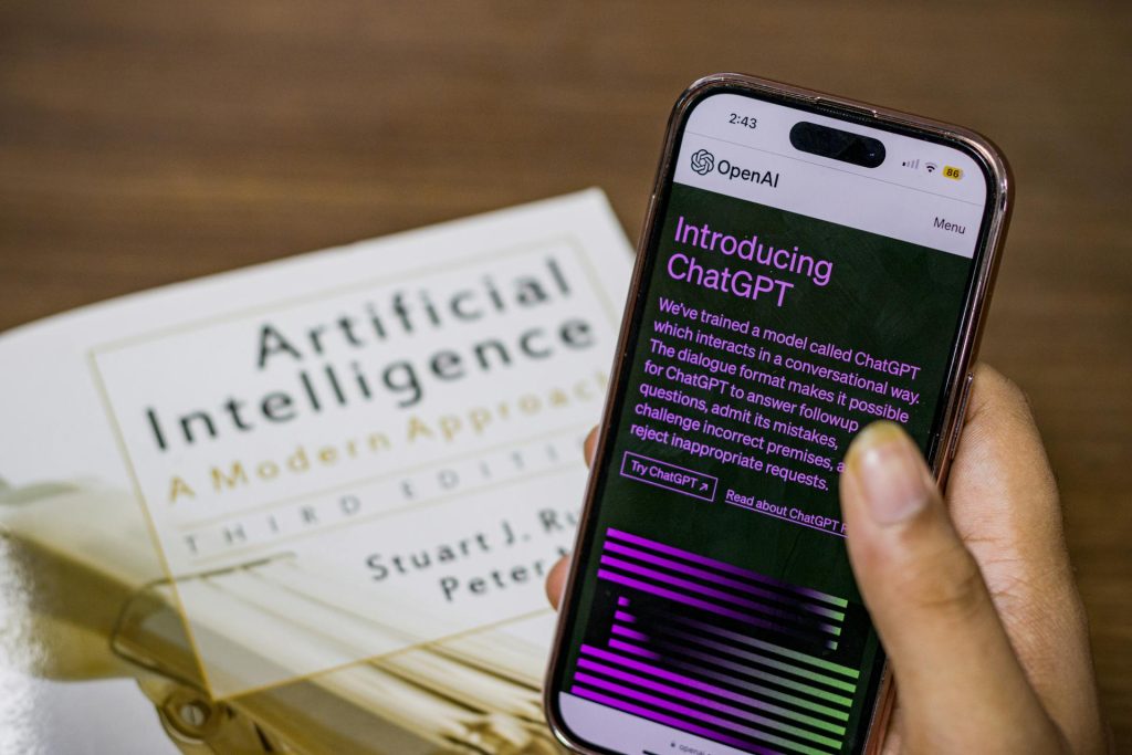 An image of a user holding up an AI chatbot on their phone while a book called "AI" is in the background.